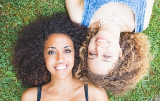 Two girls lay by each other with curly hair.