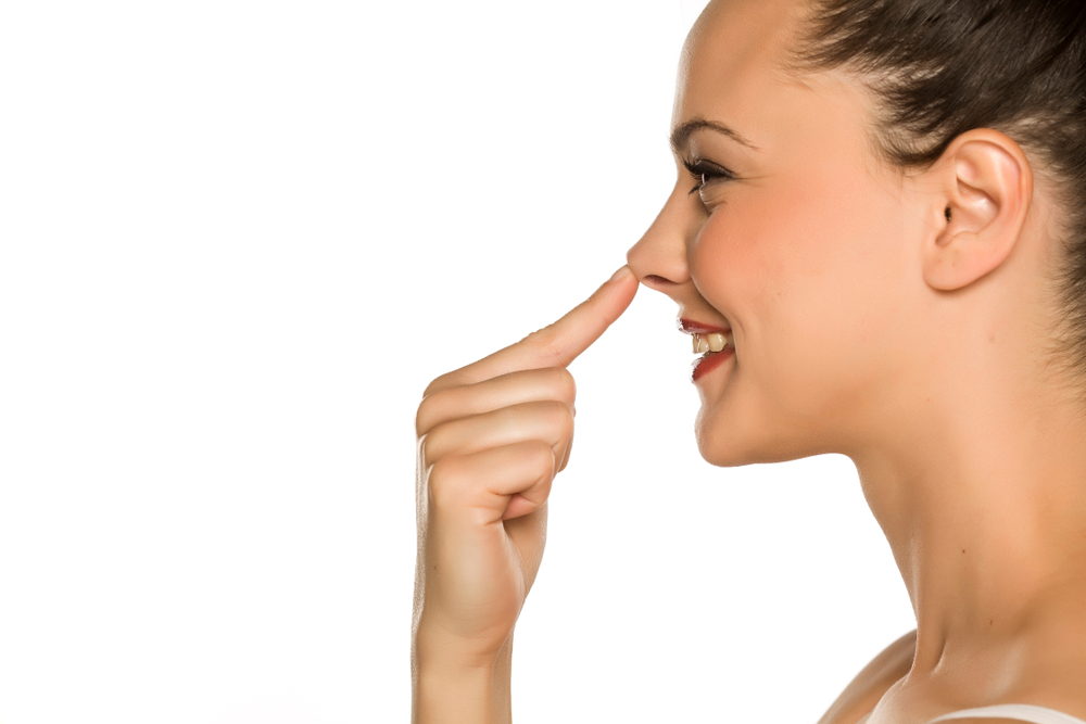 Side profile of girl happily pointing to nose after receiving a nose job.