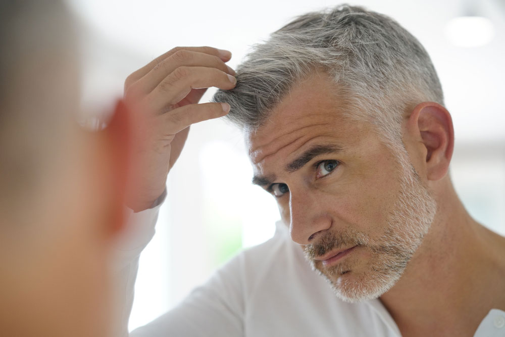 Man looking in mirror, worrying about hair loss