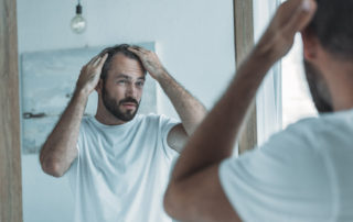 Man in need of hair restoration noticing receding hairline in mirror
