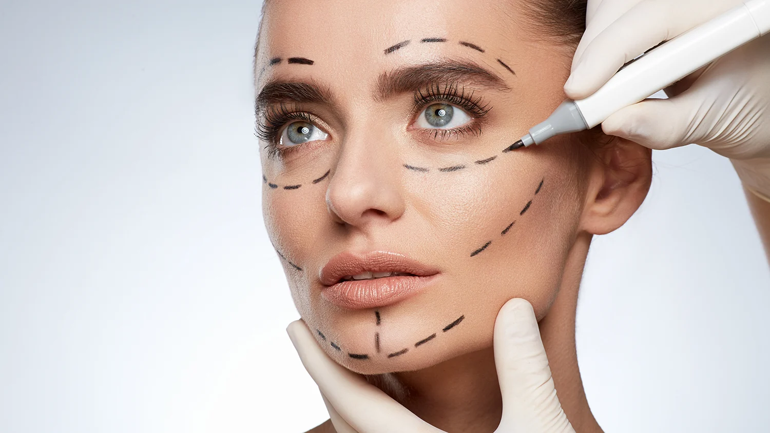 choosing a plastic surgeon involves doing some research. Pictured here: a woman at a consultation getting marks on her face.